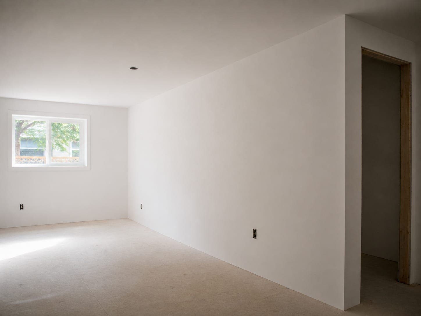 The same room after finishing, walls flat and smooth under a uniform coat of white primer with no visible seams