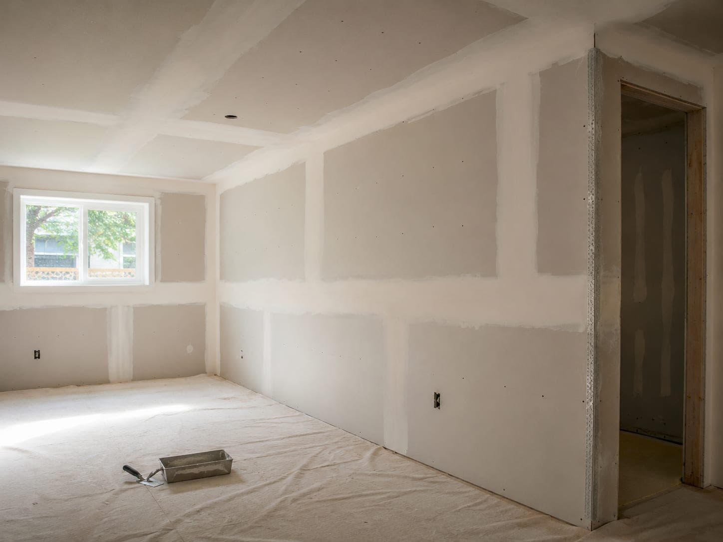 Room with newly hung drywall, seams taped and covered in fresh joint compound, metal corner bead on the outside corner
