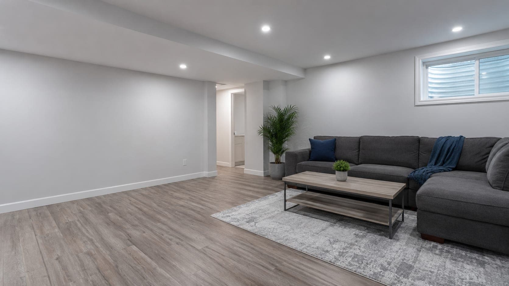 A finished basement family room with plank flooring, painted walls and recessed lighting