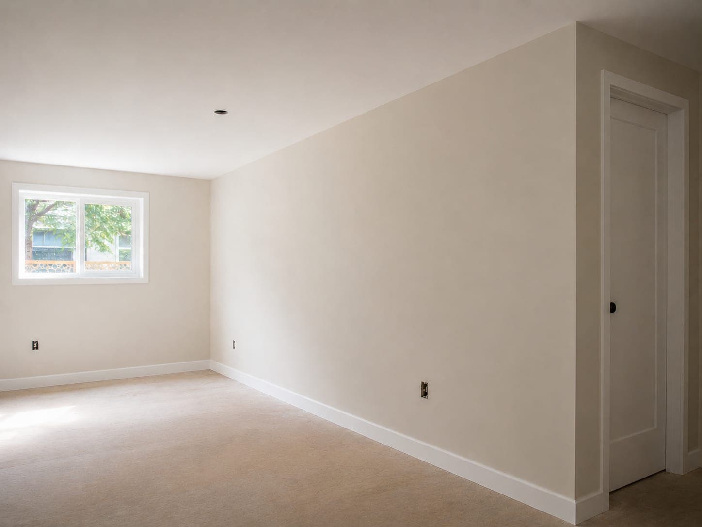 The finished room with even off-white walls, crisp cut lines at the ceiling, and painted white trim and door